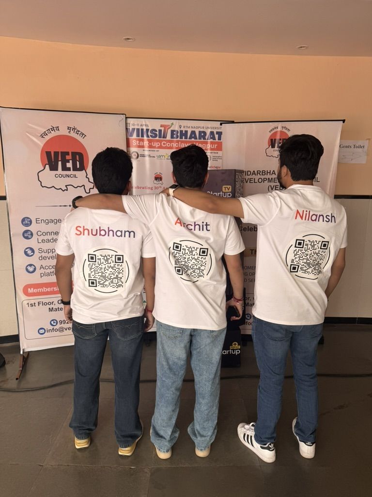 Shubham, Archit, and Nilansh showing Nimitai QR codes on the back of their branded t-shirts at Viksit Bharat Conclave Nagpur